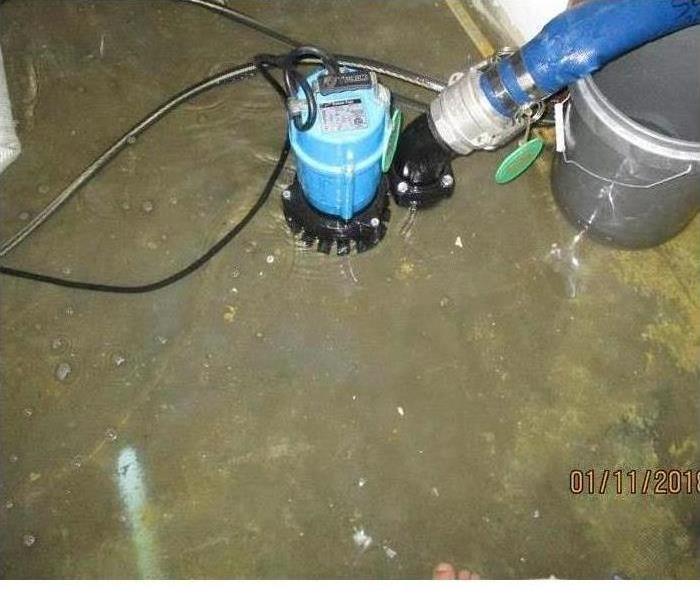 blue portable pump and hose extracting water from a floor